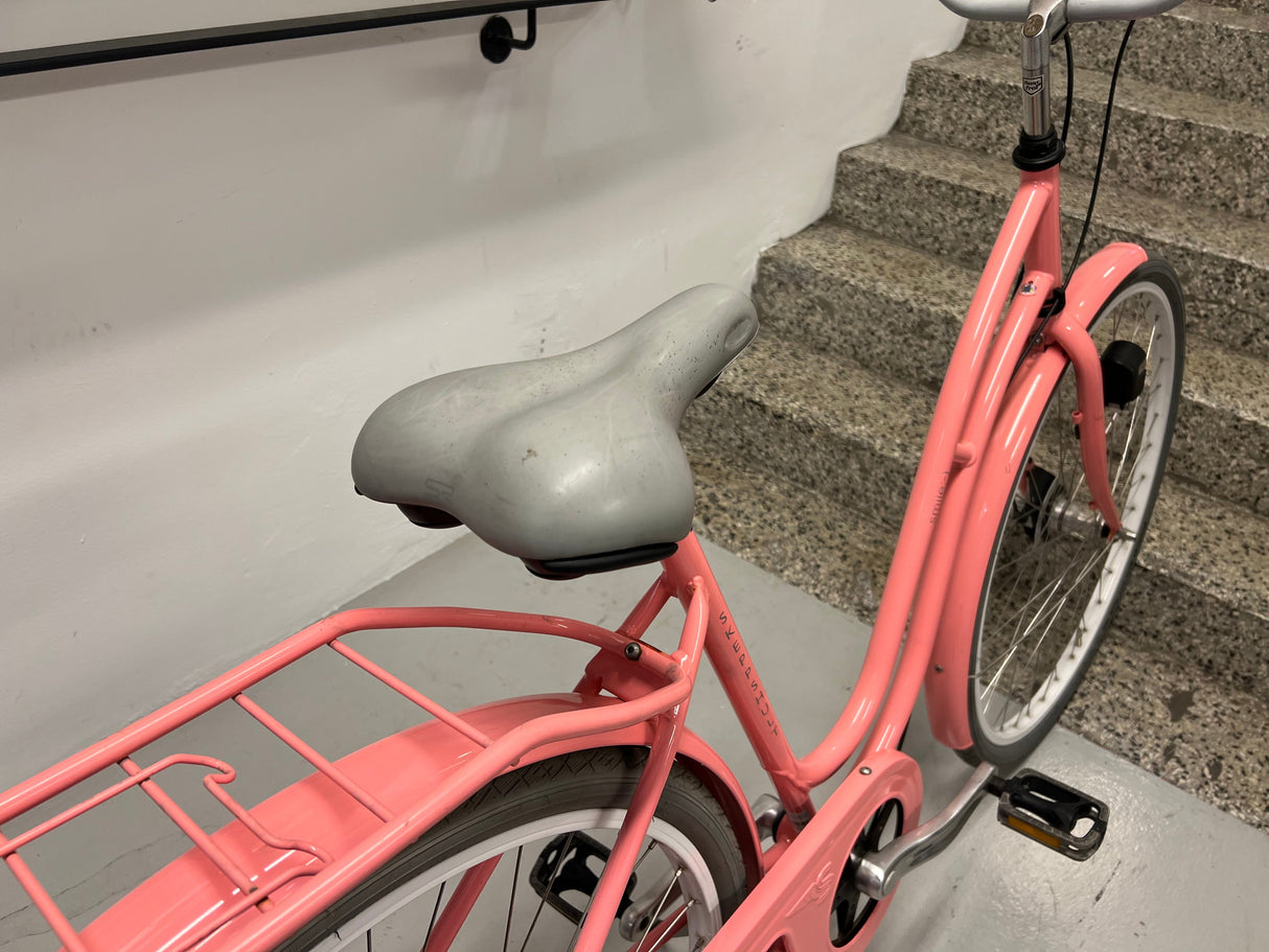 Rosa cykel med grå sittdyna och bakre pakethållare på inomhustrappa