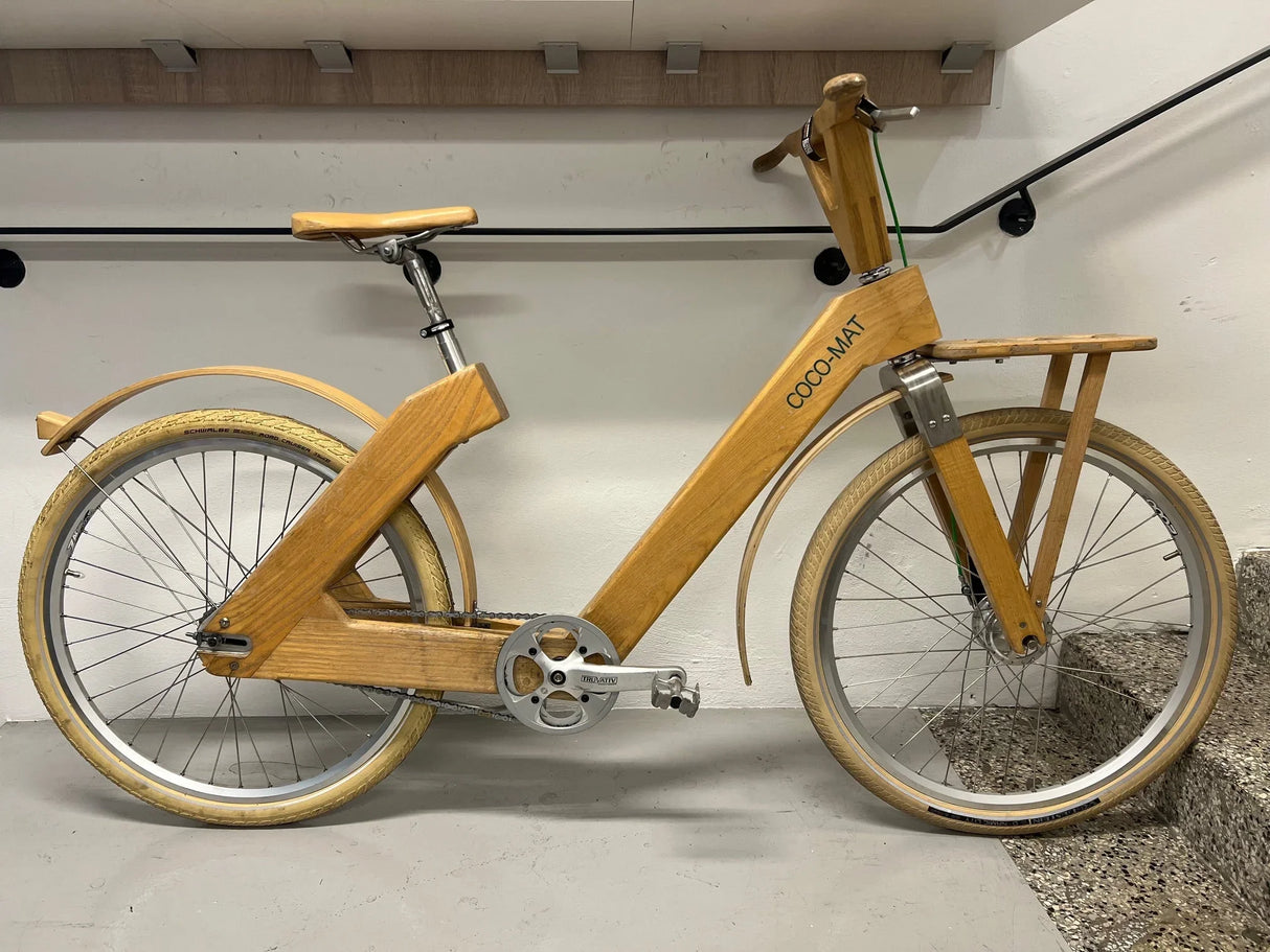 Unik träcykel med beige däck, trampor och styrstång, märkning COCO-MAT på ramen.