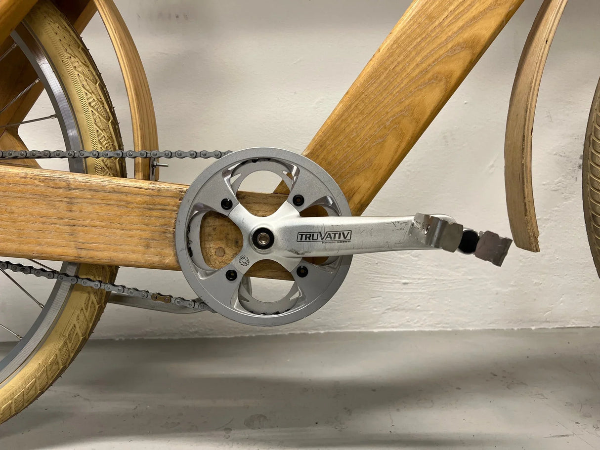Närbild på cykel vevparti och pedaler i metall, träram och beige däck på cykel