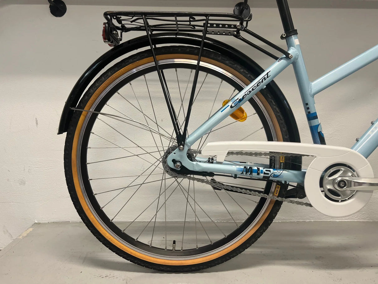 Bakre del av ljusblå Crescent cykel med beige däcksidor, kedjeskydd och pakethållare