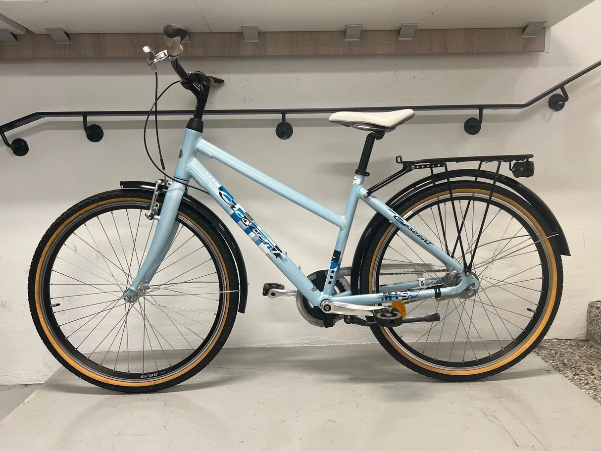 ljusblå citycykel med vit sadel, svarta skärmar och pakethållare