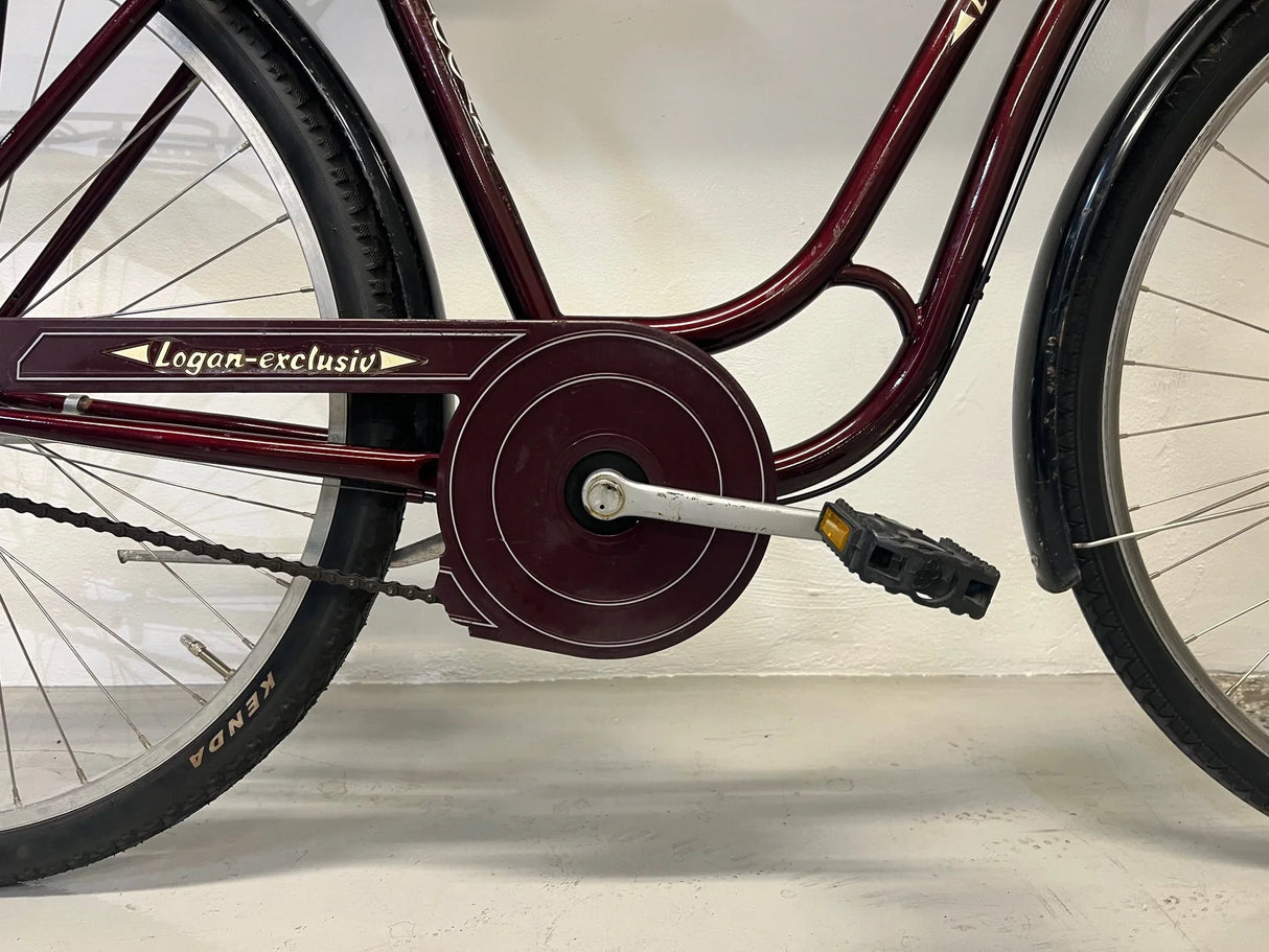 Närbild av vinröd Logan-exclusiv cykel med kedjeskydd och pedaler