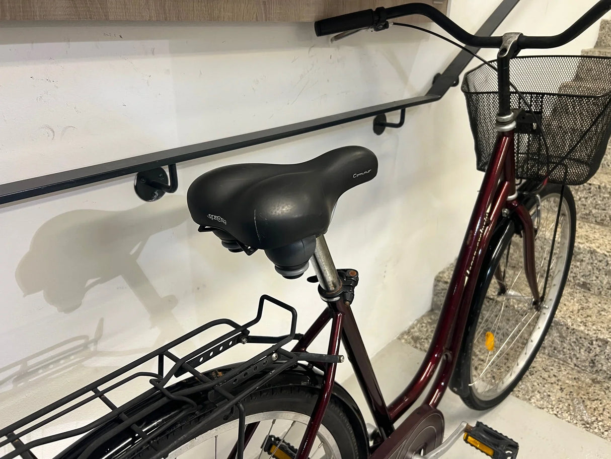 Vinröd citycykel med svart sadel, korg och pakethållare, inomhus vid trappa