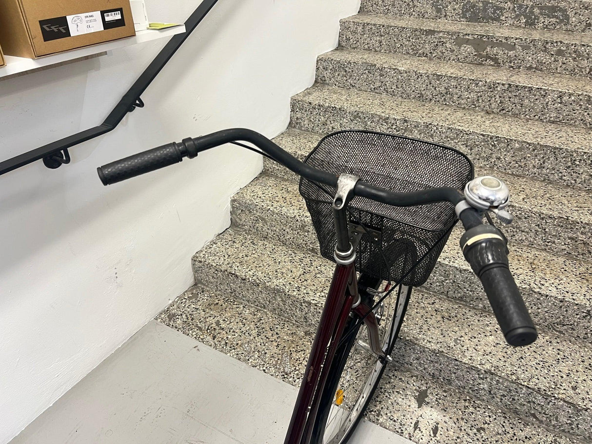 Framdel av cykel med svart styre, korg och ringklocka vid betongtrappa