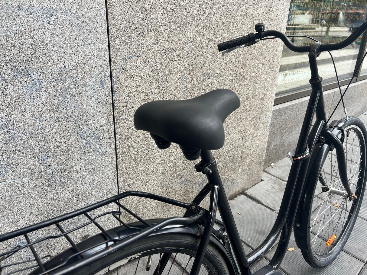 Svart stadscykel med pakethållare och bekväm sadel vid trottoar