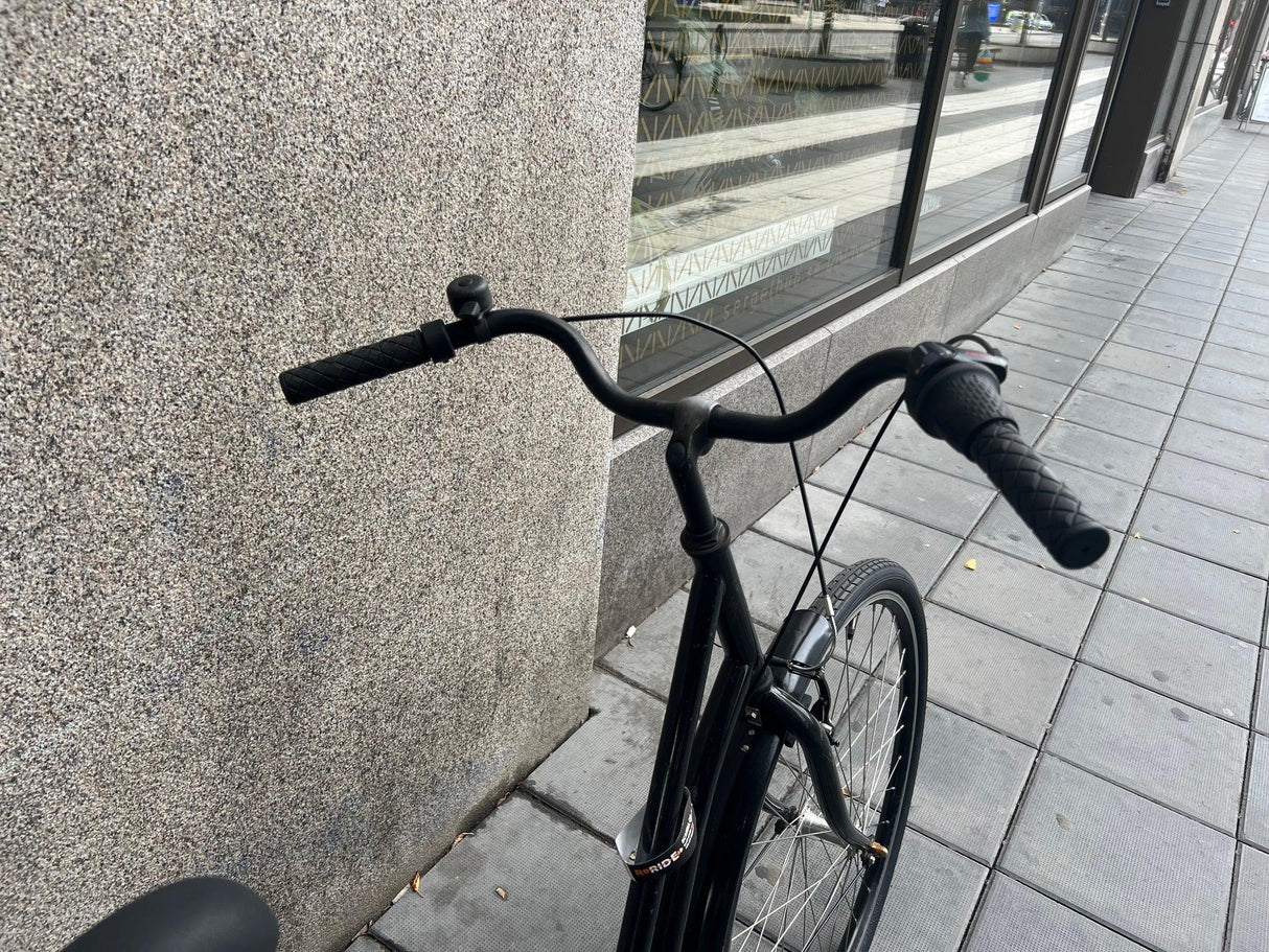 Svart cykel med räfflat styre och framdäck på trottoar av gatsten
