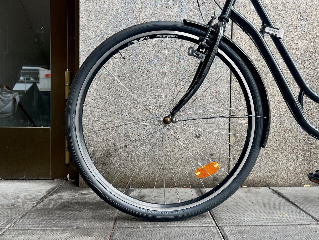 Framhjul på svart stadscykel med orange hjulreflektor och smal däckprofil
