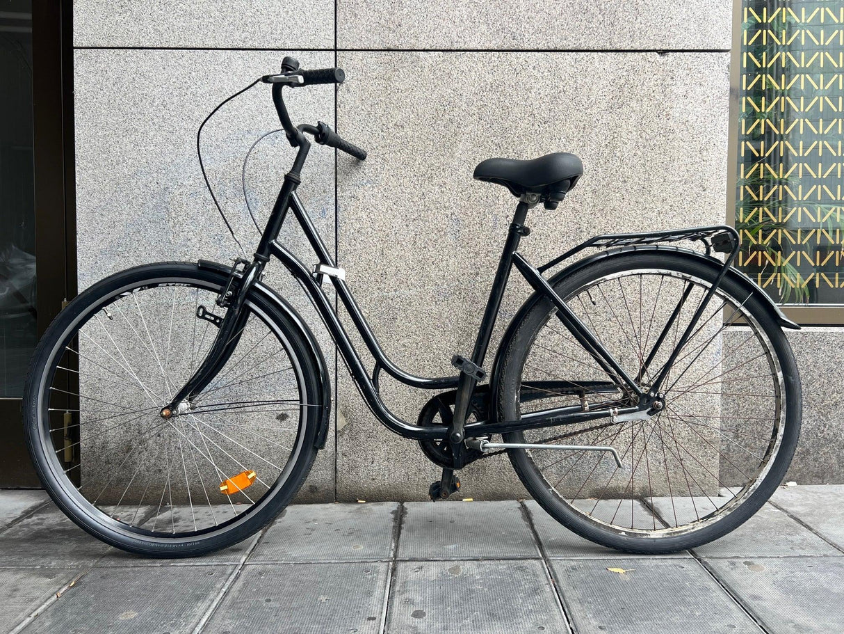 Svart citycykel med lågt insteg, pakethållare och reflex på framhjulet