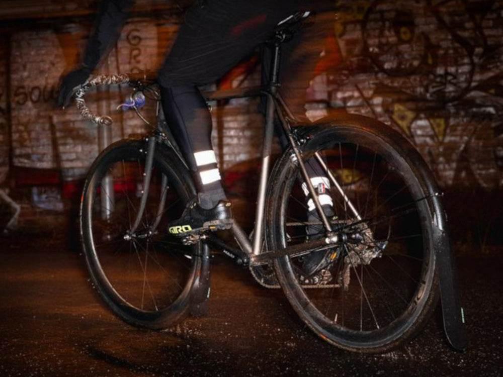 cyklist med reflexer på svarta kläder som cyklar på svart cykel med skärmskydd bak