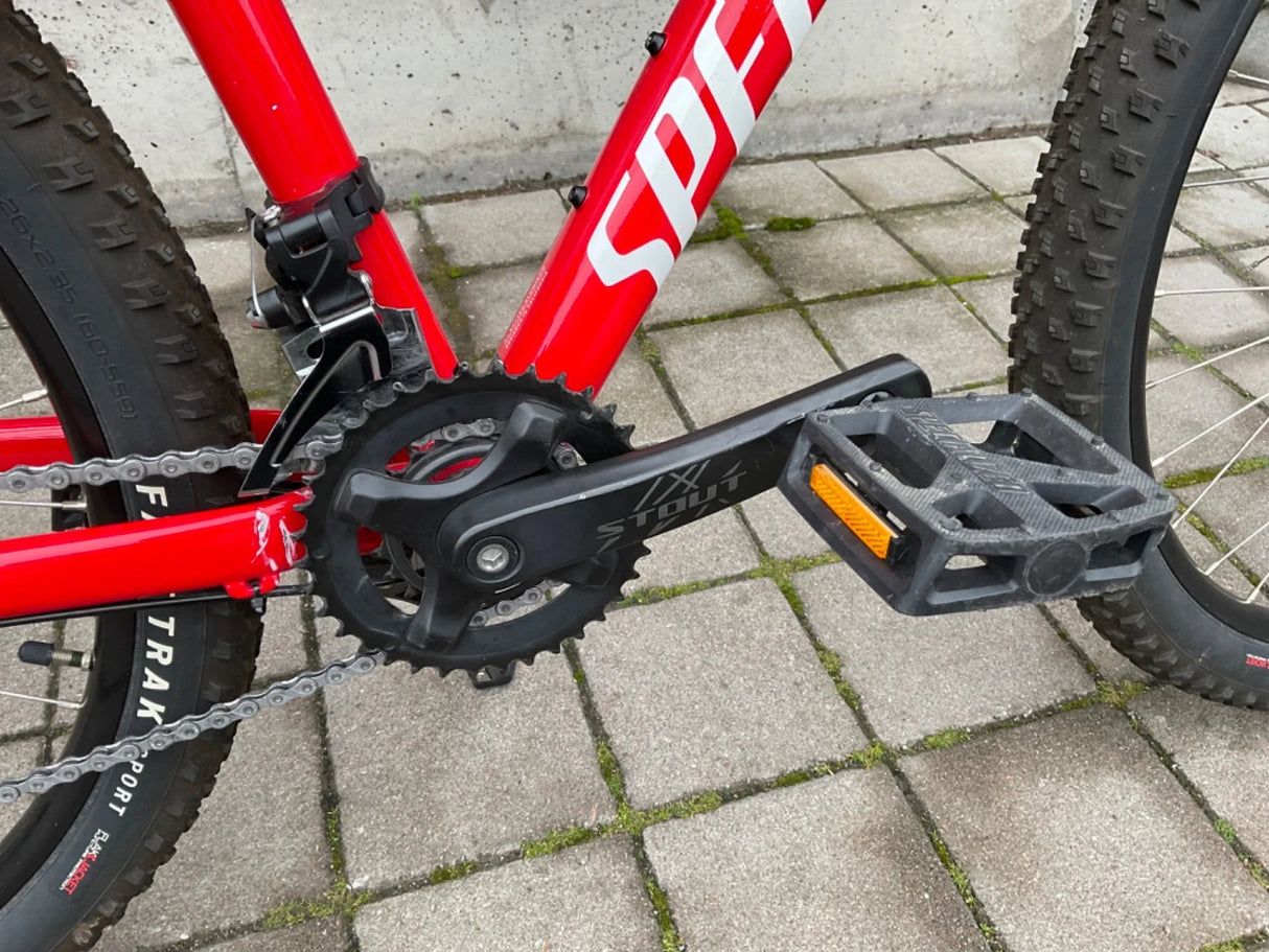 Röd mountainbike med svart pedal, kedja, och växeldel nära framdäck