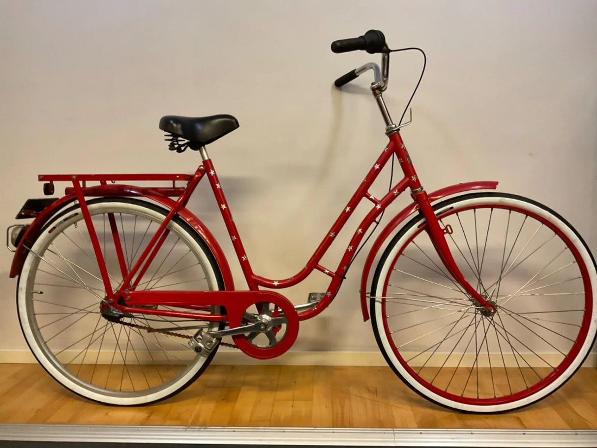 Röd damcykel med stjärnmönster, svart sadel, vita däck och pakethållare