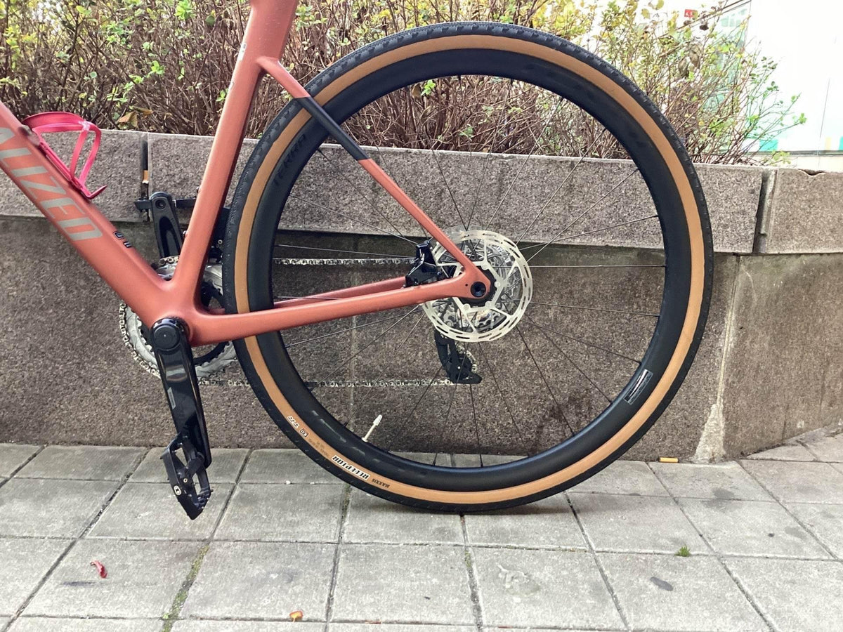 Bakre cykelhjul med bruna däck, svart vevarm och kedja på rosa Specialized cykel