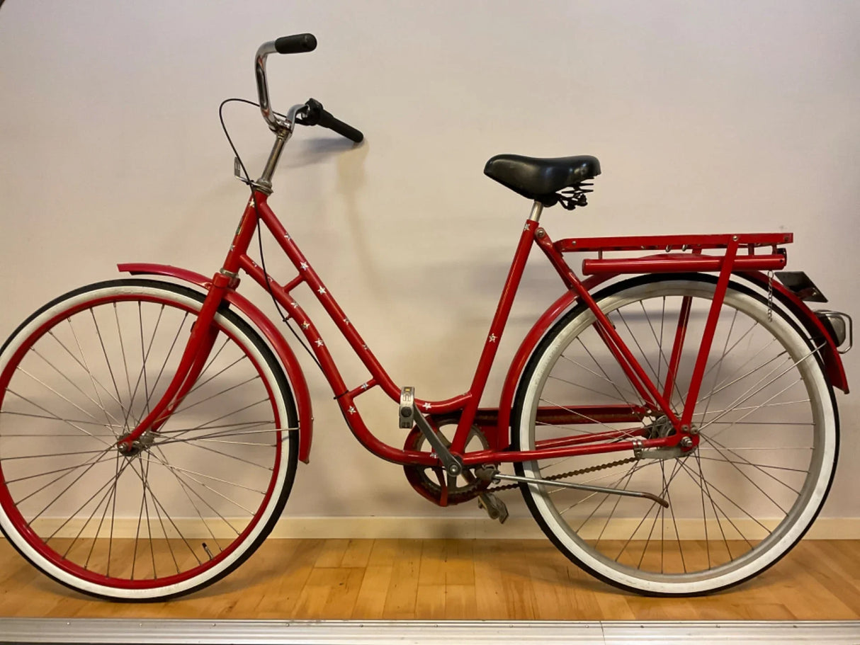 Röd damcykel med vitrandiga däck, svart sadel och pakethållare