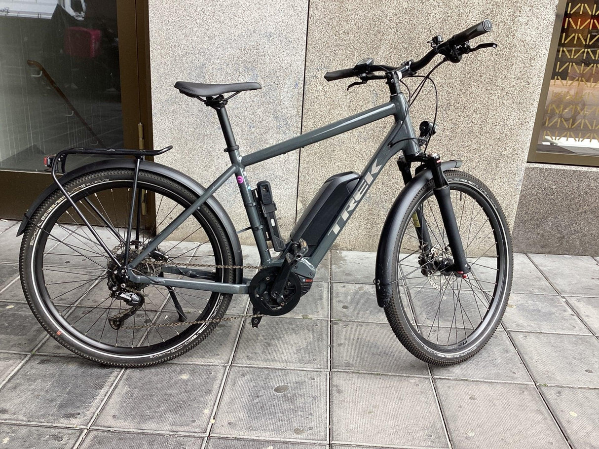 Grå elcykel Trek med Bosch motor, skärmar och pakethållare på stadsgatan