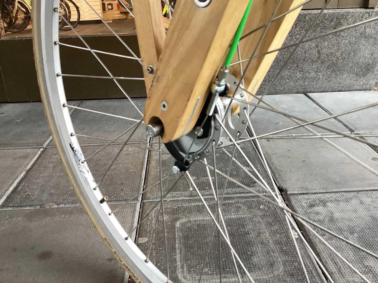 Närbild på cykelhjul med trägaffel och grönt bromsvajer, silverfärgade ekrar och vit däckkant