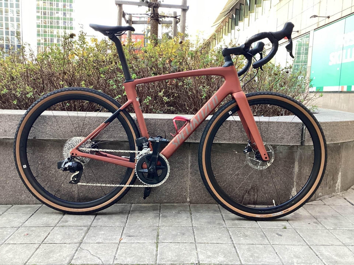 Specialized racingcykel i matt röd med tan-däck och karbonhjul, stående på stenplattor