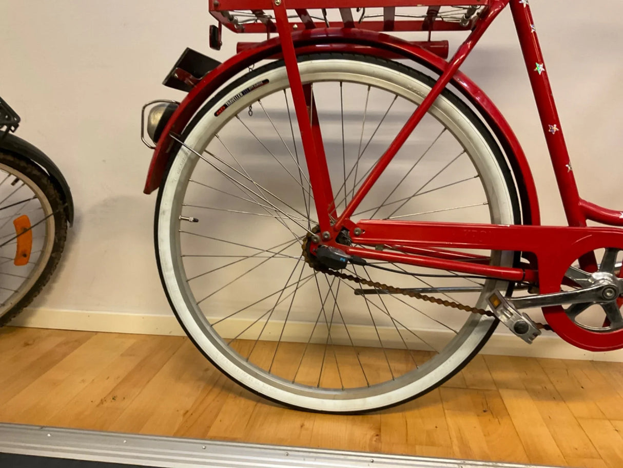 Rött cykelhjul med vit kant, kedja och pedal på trägolv