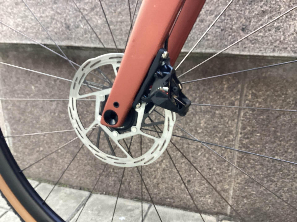 Närbild av cykelns framhjuls bromsskiva och bromsok i svart och röd ram