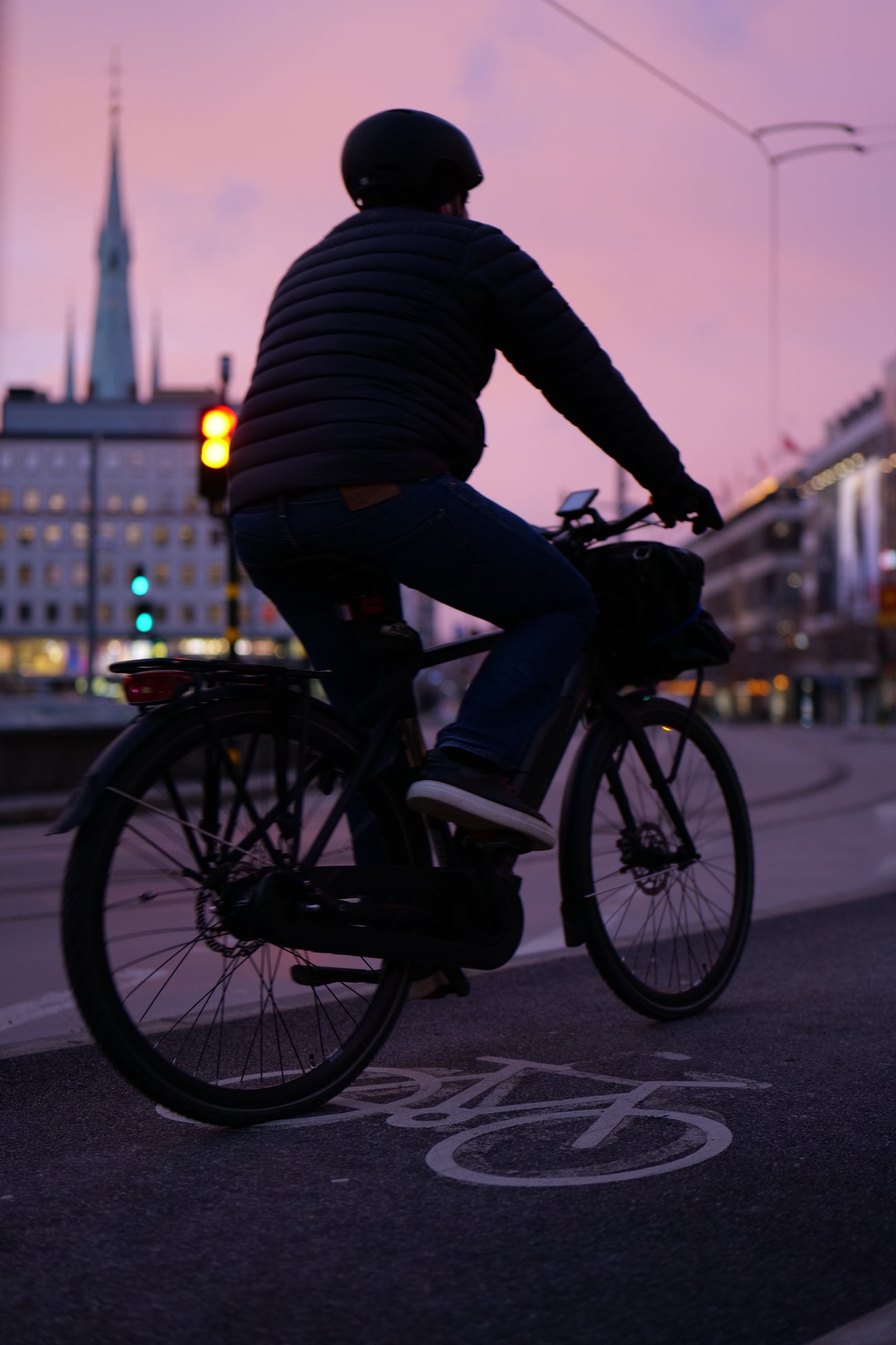 Cyklist med hjälm på elcykel vid trafikljus, cykelbana, kväll