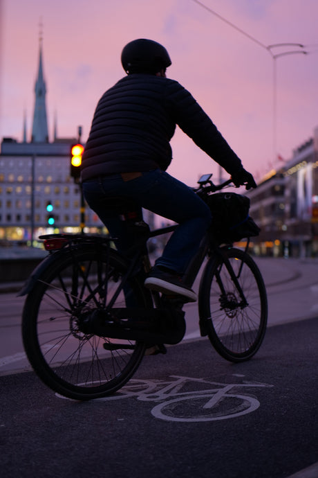 Cyklist med hjälm på elcykel vid trafikljus, cykelbana, kväll