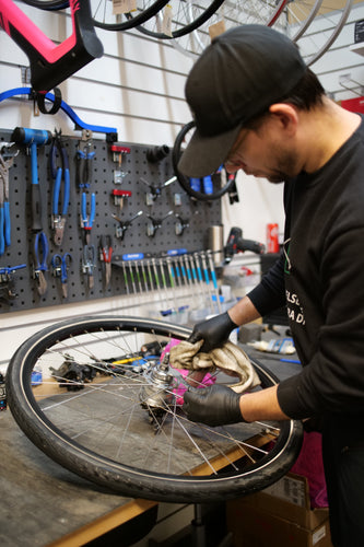 Cykelreparatör rengör cykelhjul och växlar, cykelverkstad, verktyg på vägg