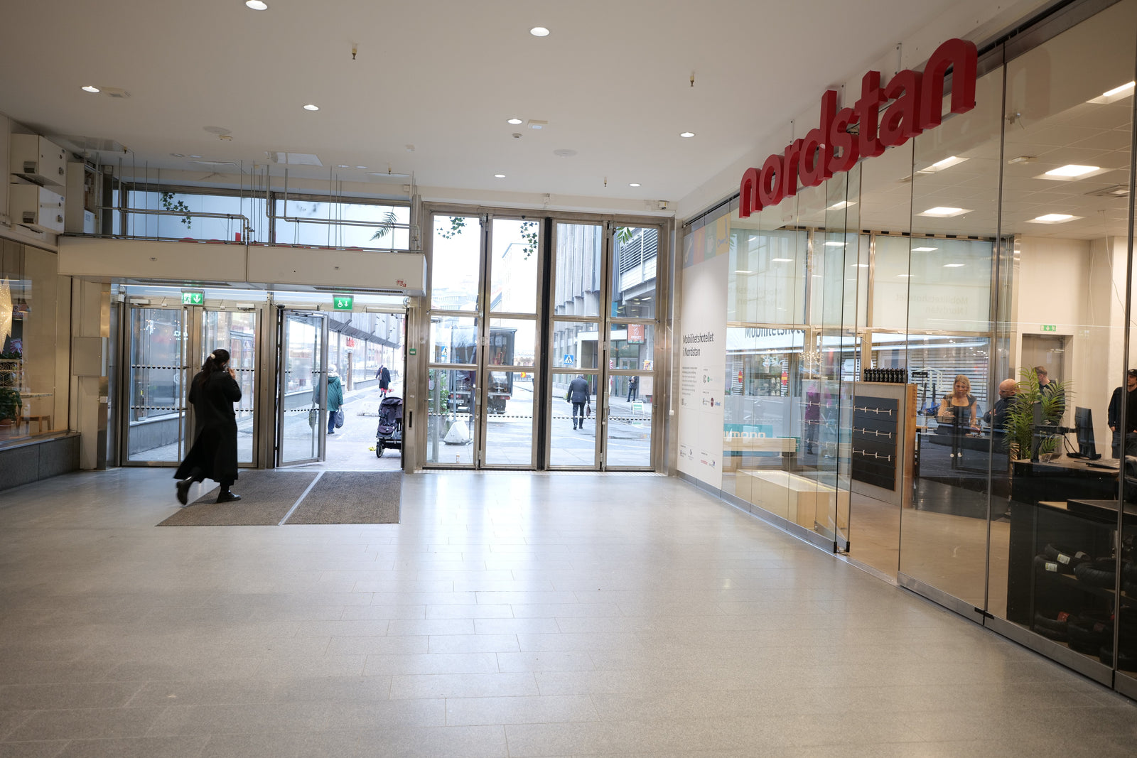 Entré nordstan, kvinna i svart rock går ut, glasvägg, butiksskylt nordstan