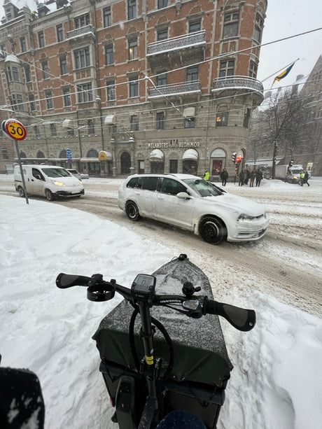 Lastcykel i snöigt väder på gata med bilar och cykelskylt, vintertrafik Stockholm