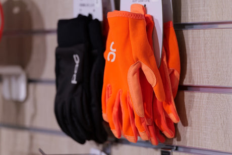 Orange och svarta cykelhandskar med logotyp, upphängda på display