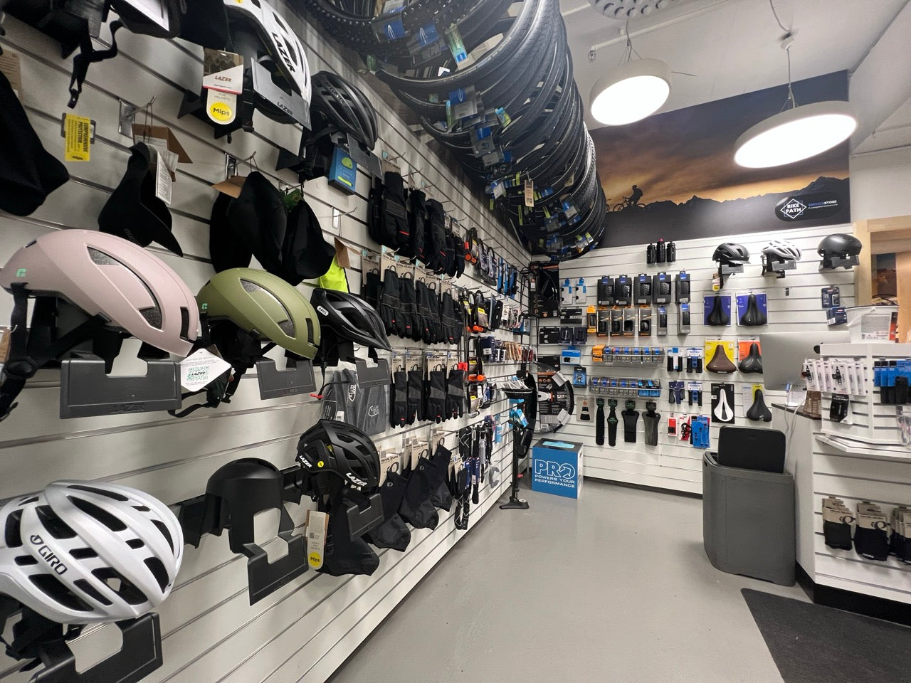 Cykelhjälmar, handskar, däck och sadlar på vägg i cykelbutik