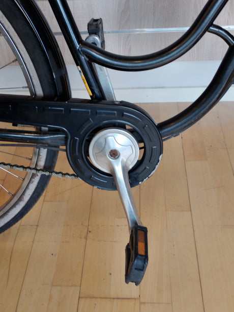 cykelpedal och vevarm i metall, kedja och svart kedjeskydd