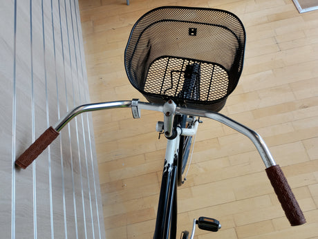 Cykelstyre med bruna grepp och svart cykelkorg fram, cykelpedal synlig