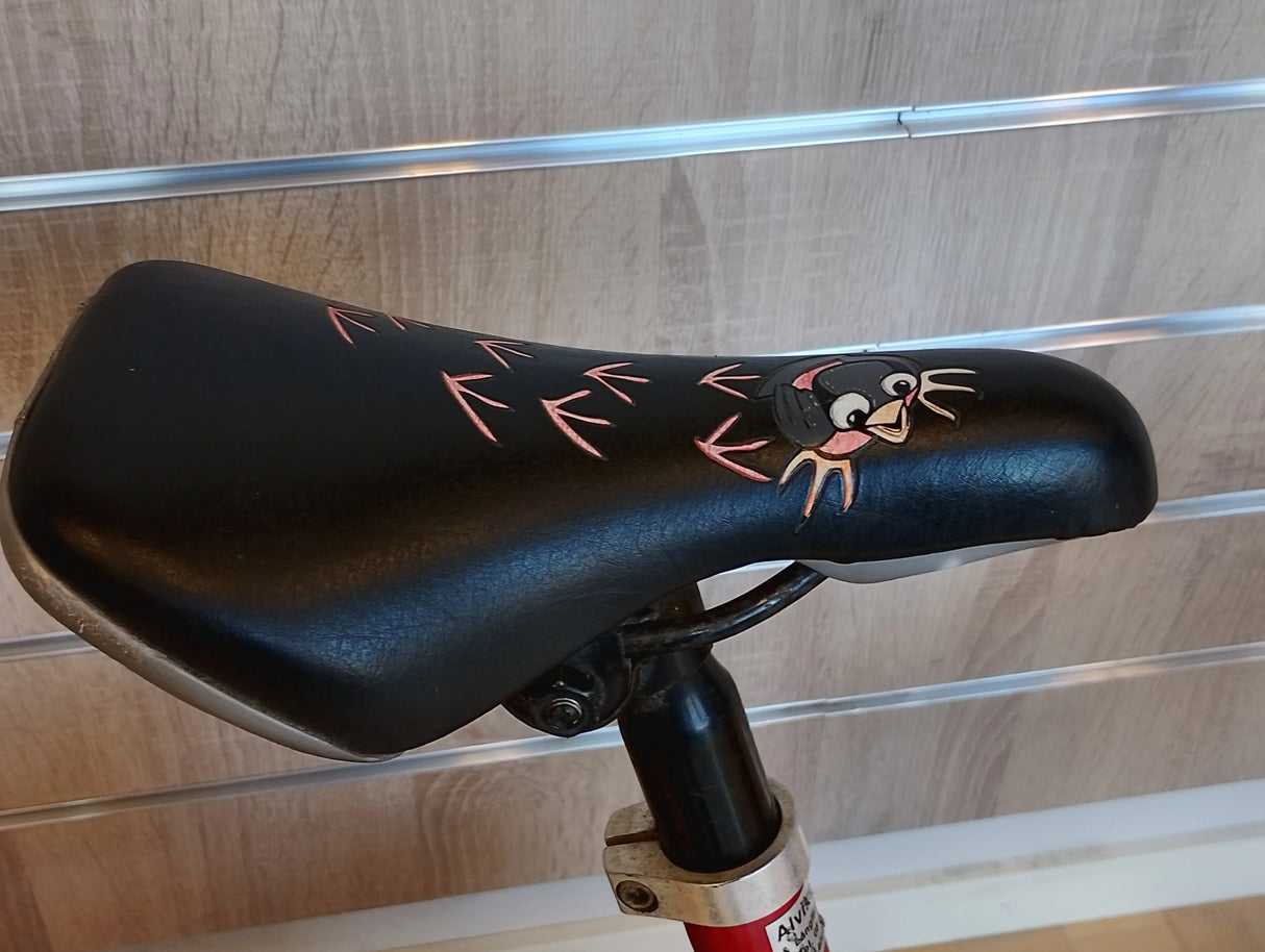 Svart cykelsadel med tecknat fågelmotiv och rosa fågelspår, barncykel tillbehör.