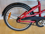 Bakdel av röd barncykel med bakhjul, kedjeskydd och reflex, närbild.