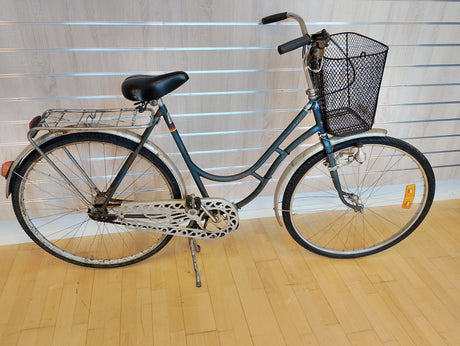 Gammal damcykel med korg, pakethållare och kedjeskydd på trägolv