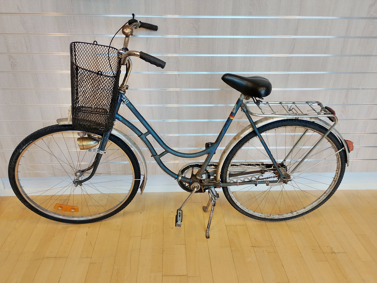Blå damcykel med korg fram och pakethållare bak, klassisk retrocykel.