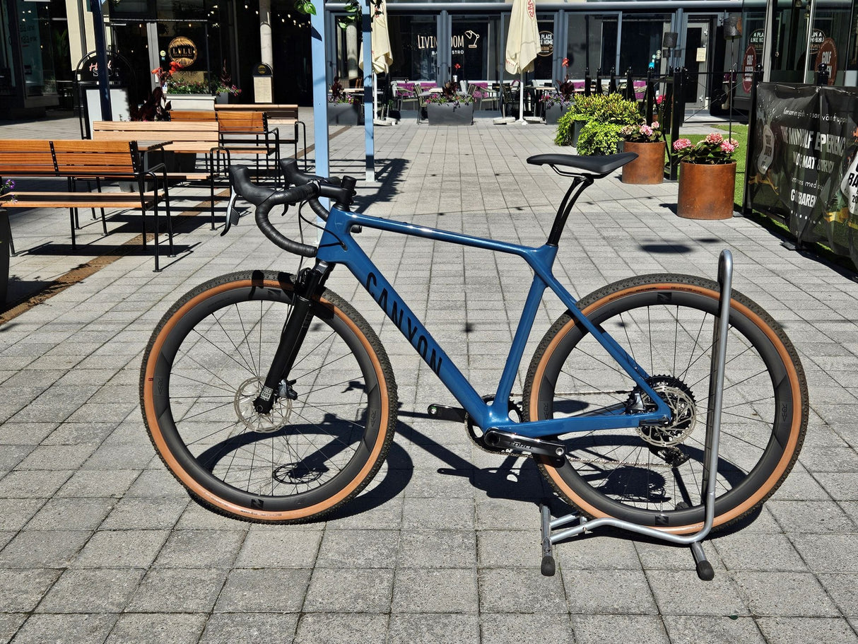 Blå Canyon gravel-cykel med breda däck, svart sadel och styre i cykelställ