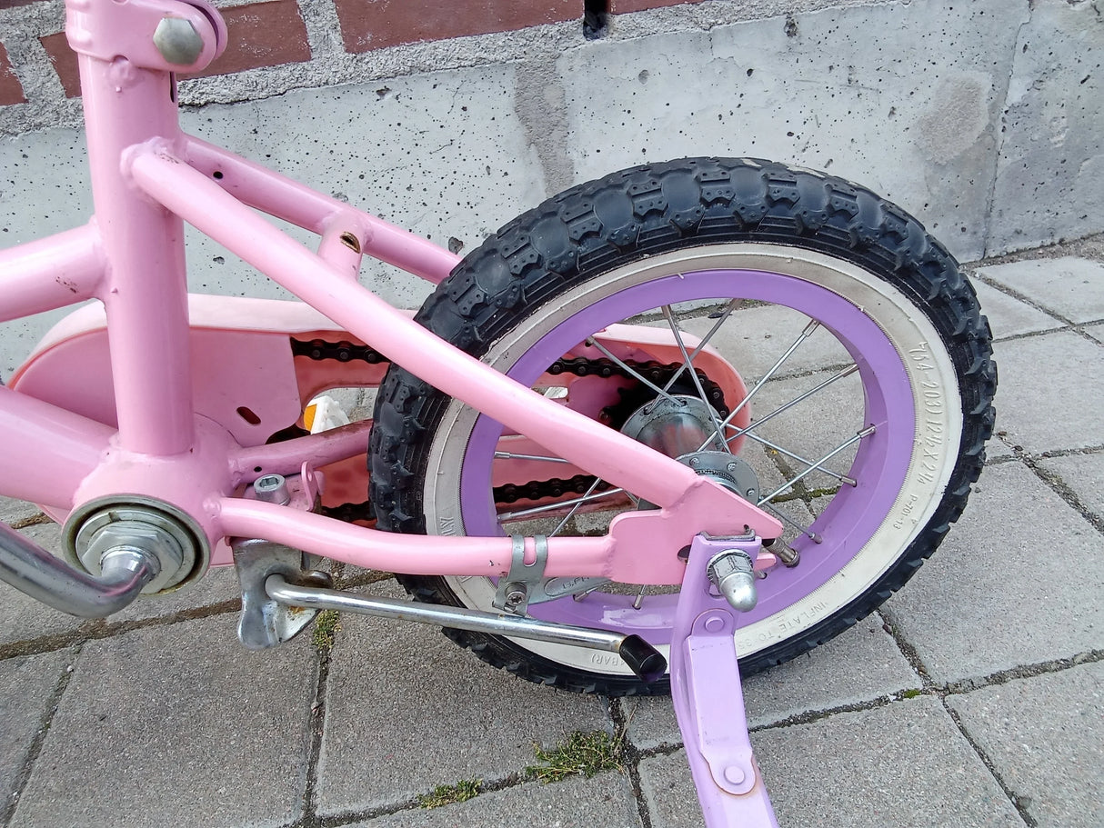 Bakre hjul och kedja på rosa barncykel med lila fälg och stödhjul