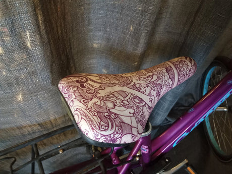 Cykelsadel med detaljerat mönster på lila cykelram med blå hjul