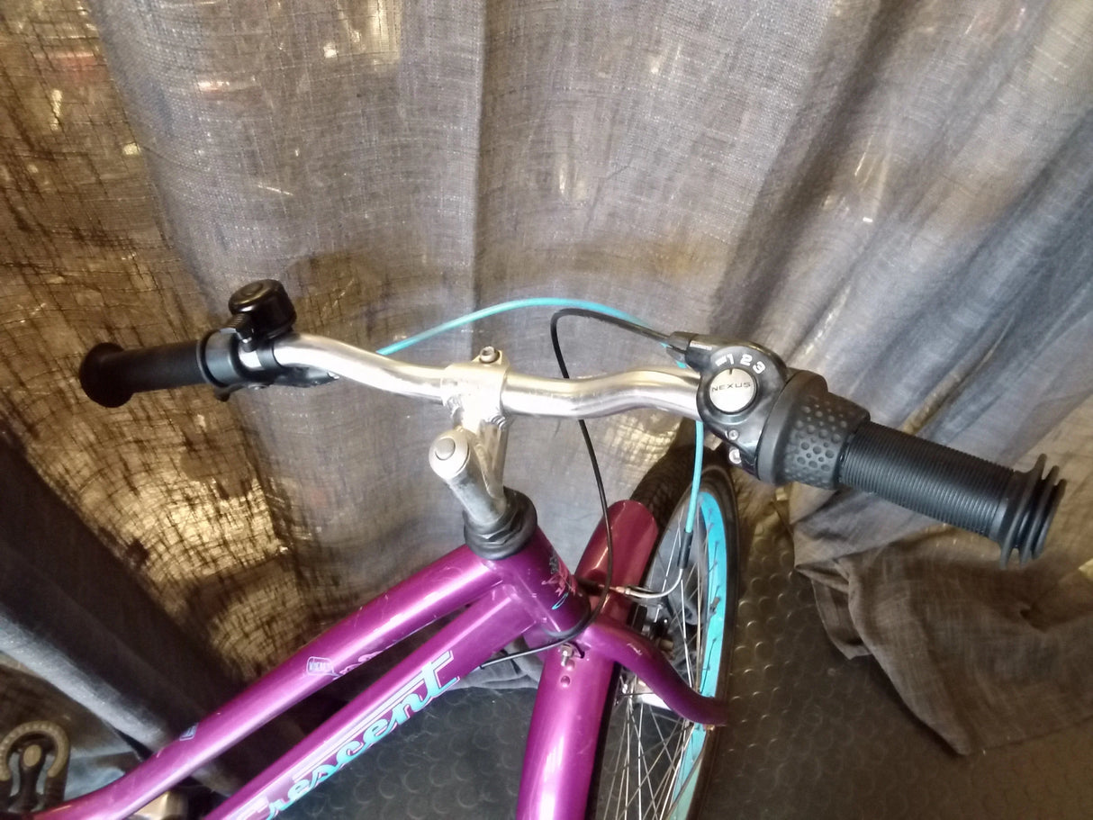 Styret på en lila Crescent cykel med svart handtag, blå bromsvajer och drev med 3 växlar