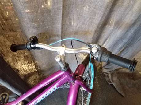 Styret på en lila Crescent cykel med svart handtag, blå bromsvajer och drev med 3 växlar