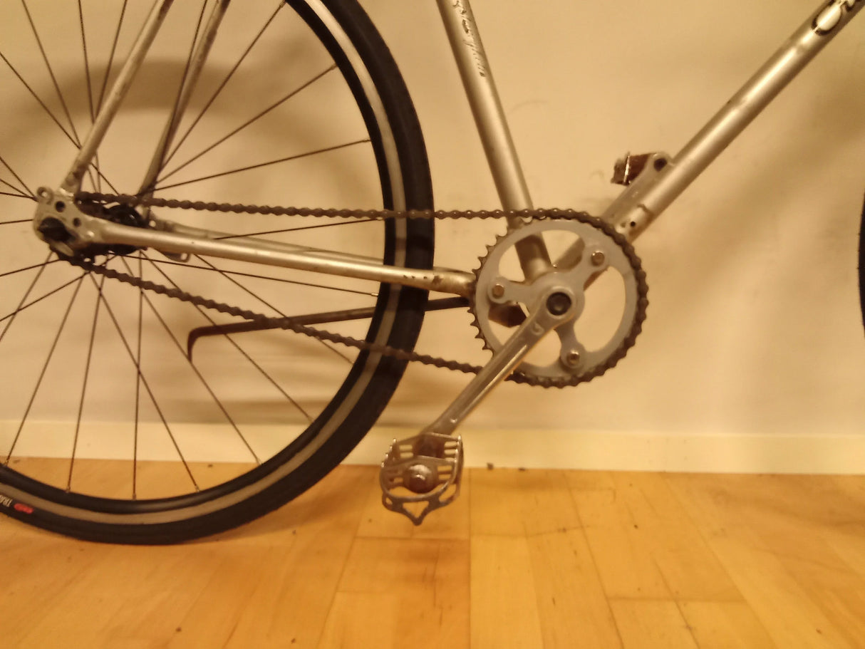 del av cykel med kedja, pedal och bakhjul på trägolv