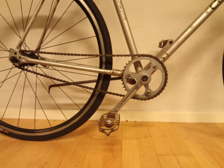 del av cykel med kedja, pedal och bakhjul på trägolv