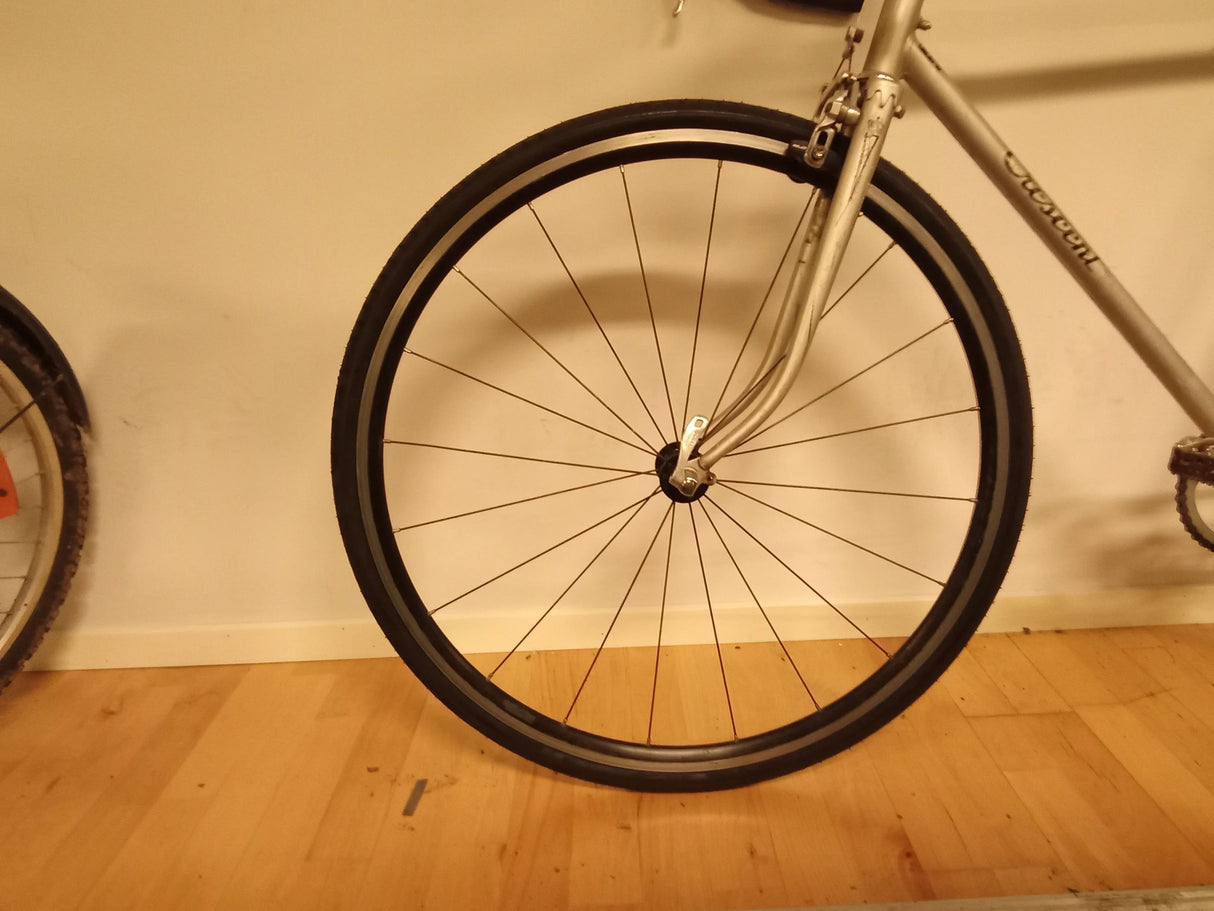 Närbild av framhjul på silverfärgad cykel med smalt däck och svart ekrar