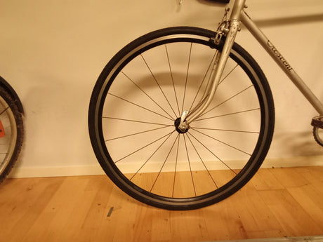 Närbild av framhjul på silverfärgad cykel med smalt däck och svart ekrar