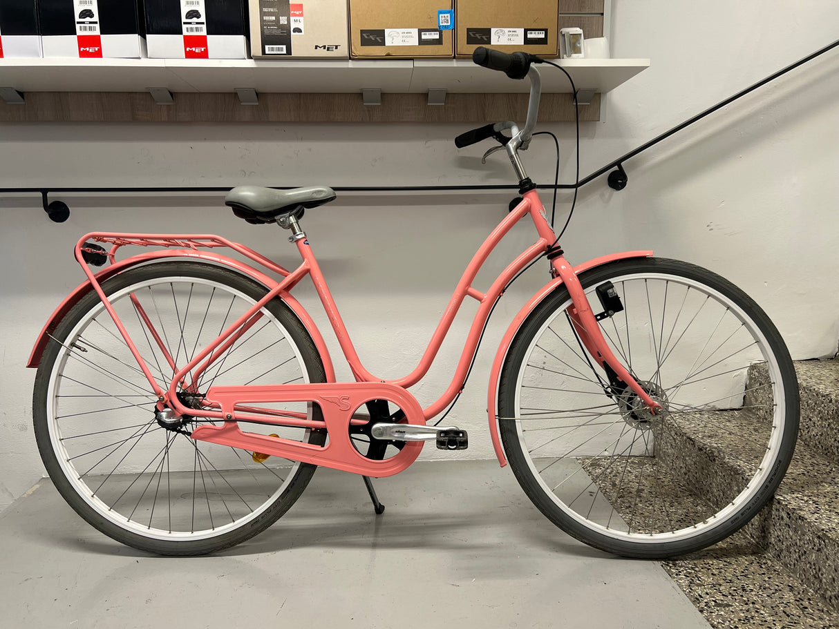 Rosa damcykel med vit sadel, svart styre och pakethållare på grått golv