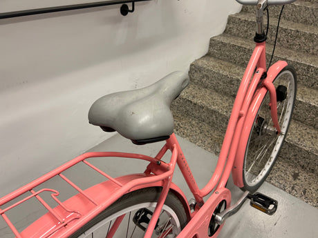 Rosa cykel med grå sittdyna och bakre pakethållare på inomhustrappa