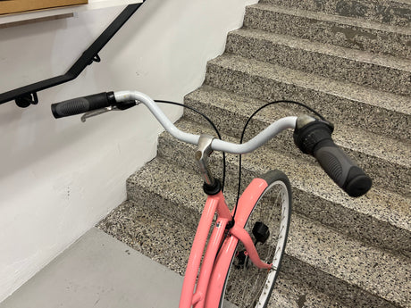 Cykel med rosa ram och vita däck med svart handtag på styret