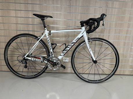 Vitt Canyon racercykel med svart sadel och styre mot träpanel