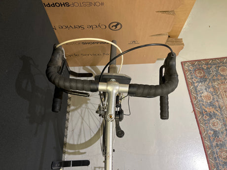 Närbild på silvergrå racercykel med svarta handtag och växelreglage