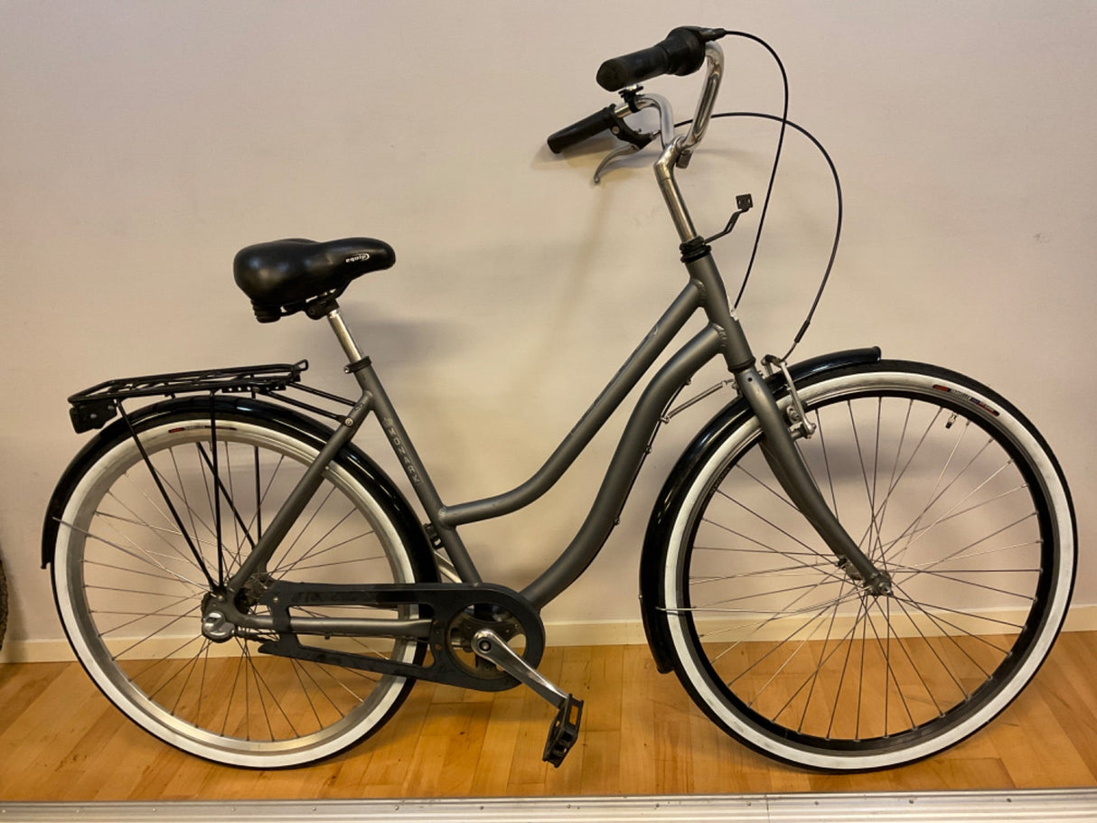 grå citybike med svart sadel, pakethållare och vita däcksidor på trägolv